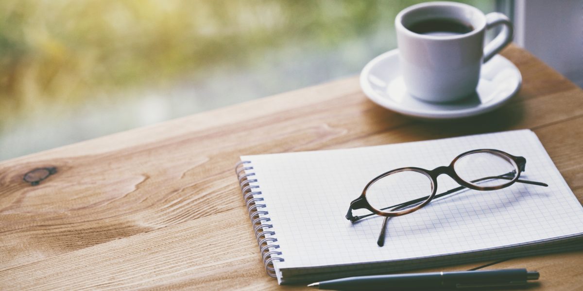 cup of fresh morning coffee with paper notebook, glasses and pen for writing