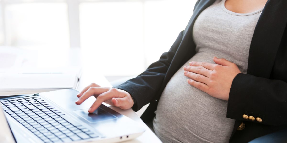 Pregnant woman working on laptop. Cropped image of pregnant businesswoman typing something on laptop while sitting at her working place in office